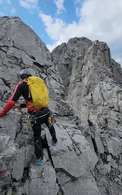 A climber nearing the top of Little Sister Mountain on exposed and loose rocky ridge.