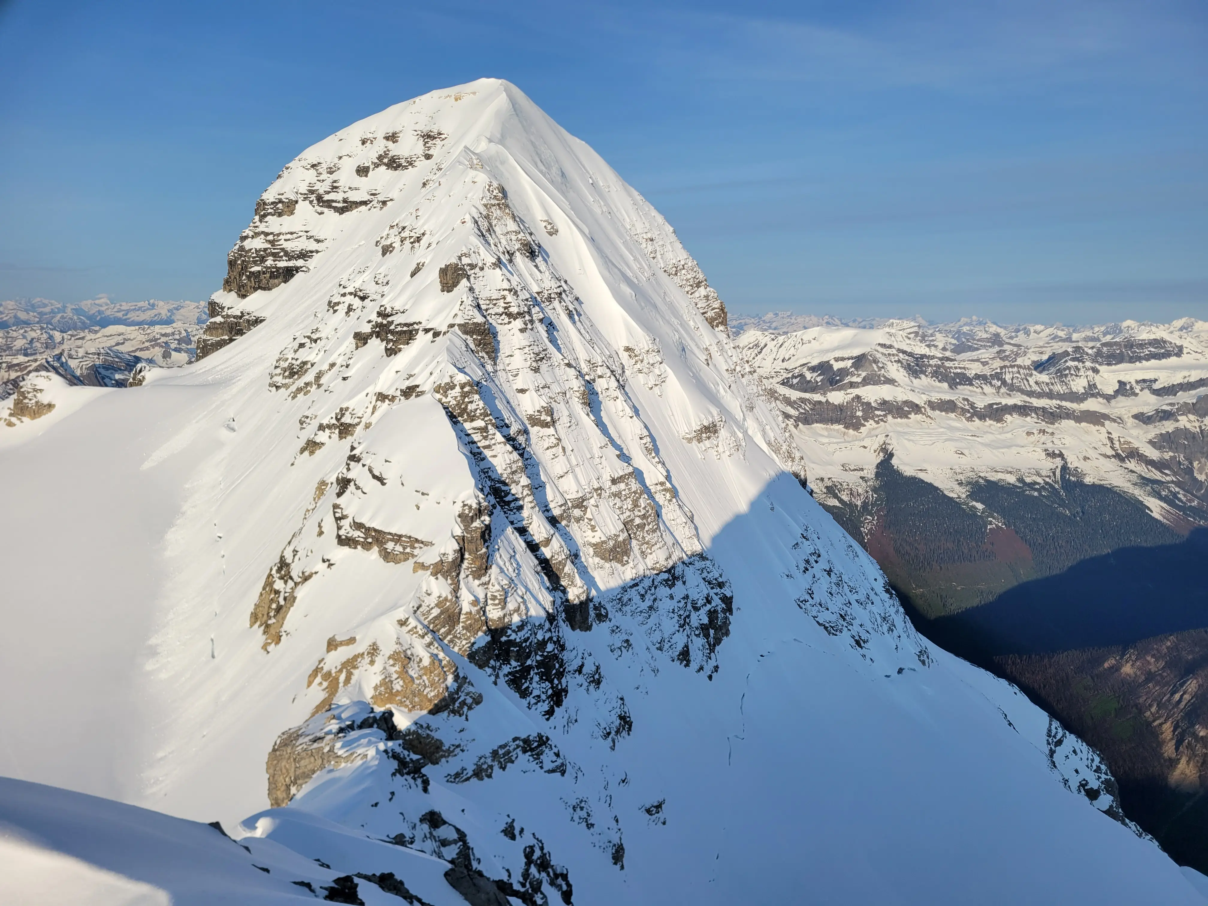 Mount Bryce in the Canadian Rockies with its steep north face in shadow and the snow-covered northeast ridge route climbing directly up the center.