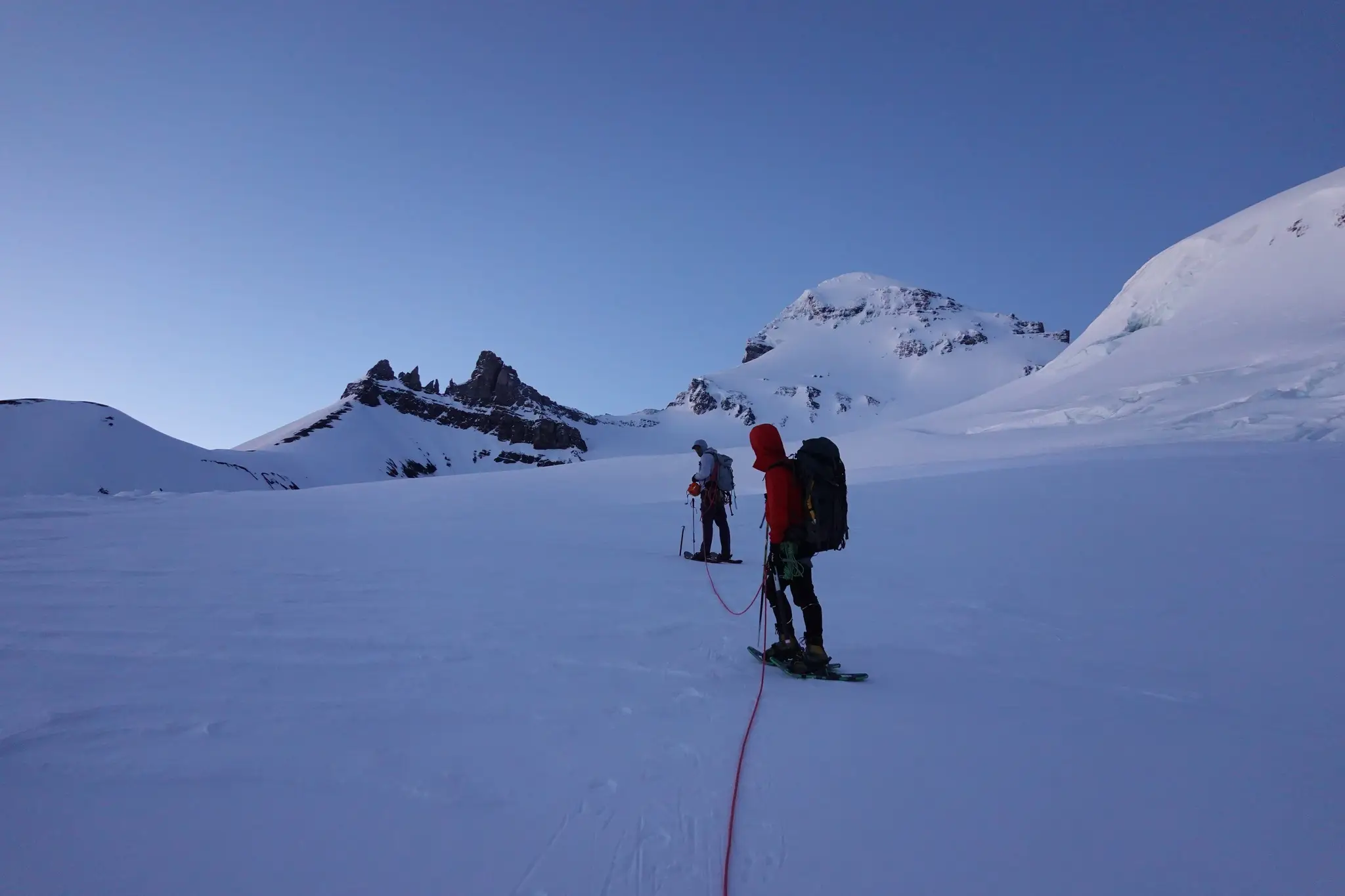 Climber on the upper flanks of Mount Forbes with it's summit block behind and a few pinnacles along one of its ridges at left.