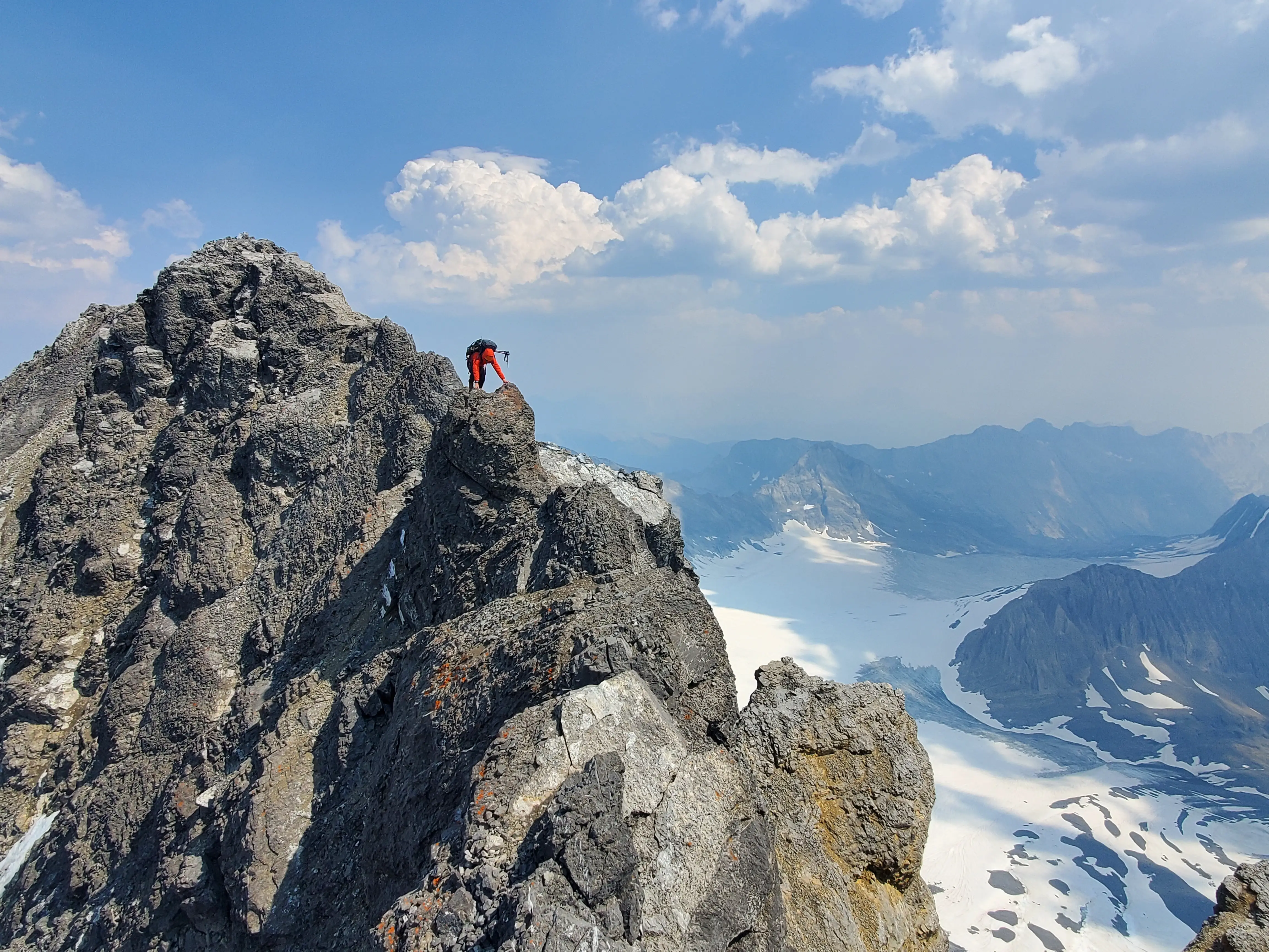 Climber descending the summit ridge of Mount Sir Douglas, climbing over the prominent pinnacle with the expansive Haig Glacier and surrounding peaks visible in the background.