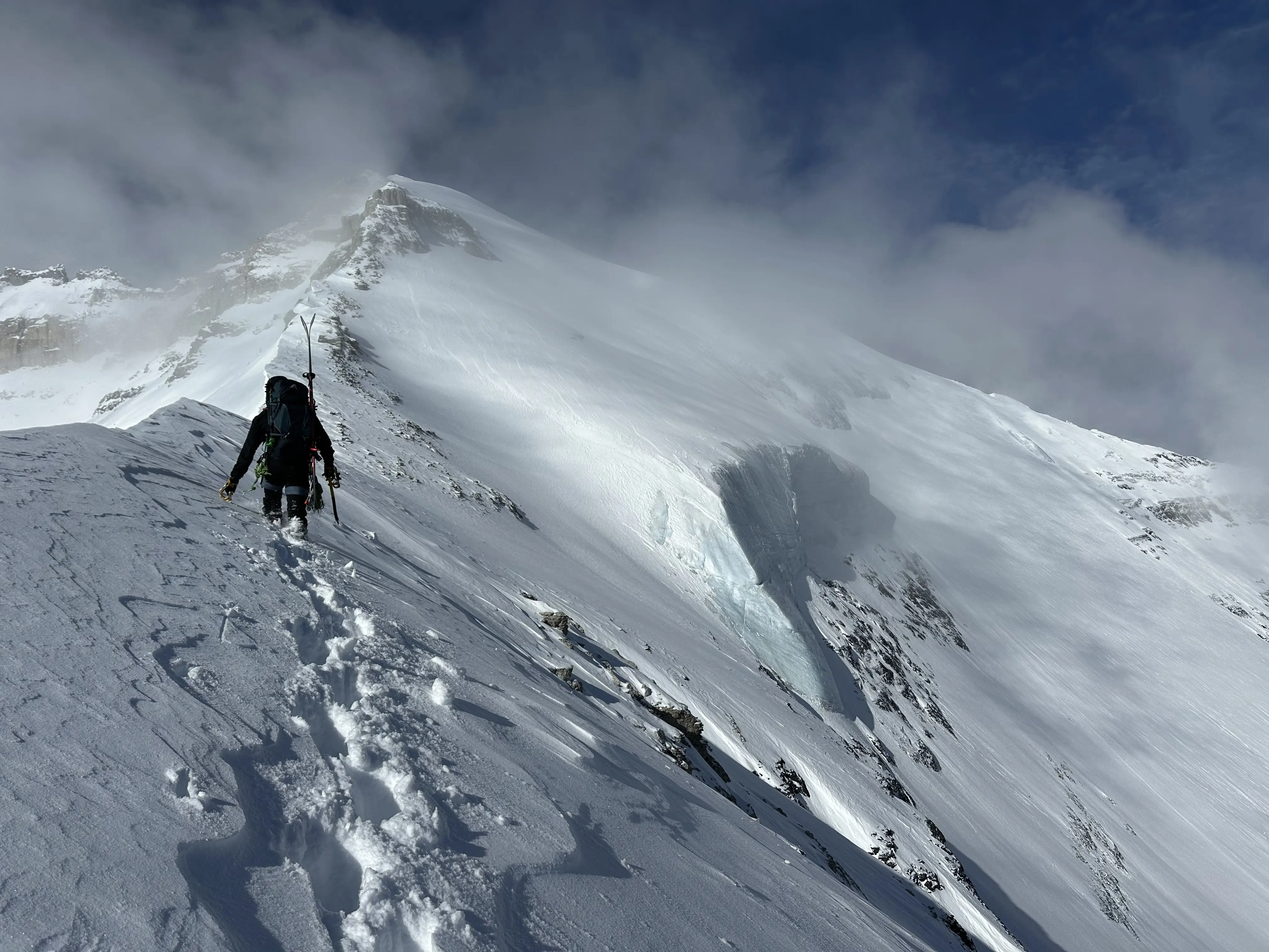 A climber ascending the NE ridge of Mount Victoria's north peak with impressive glacier visible on it's north face to the right.