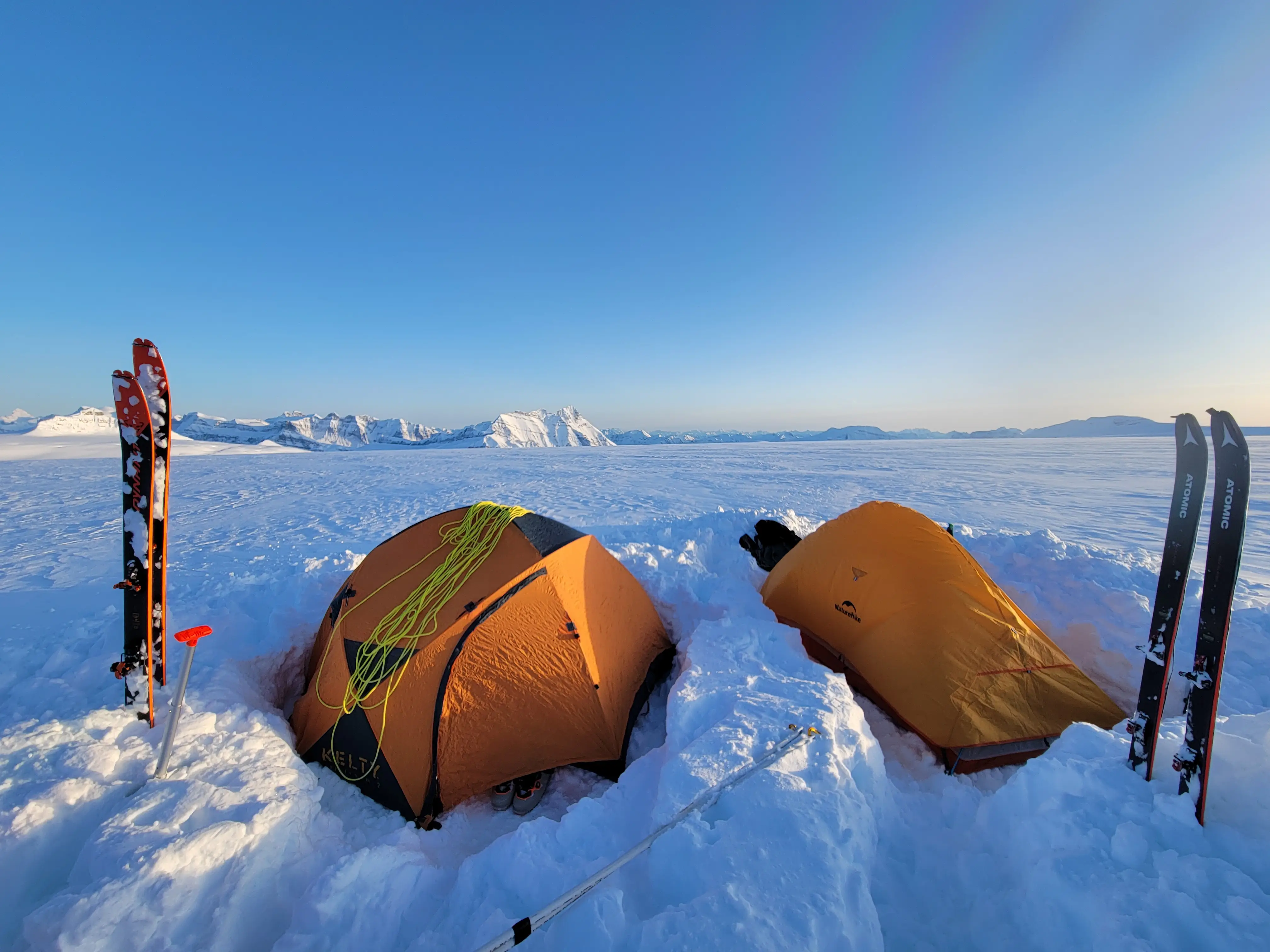 A high altitude camp on the Columbia Icefield with sunset colors, Mount Bryce on the horizon, and snow as far as the eye can see.