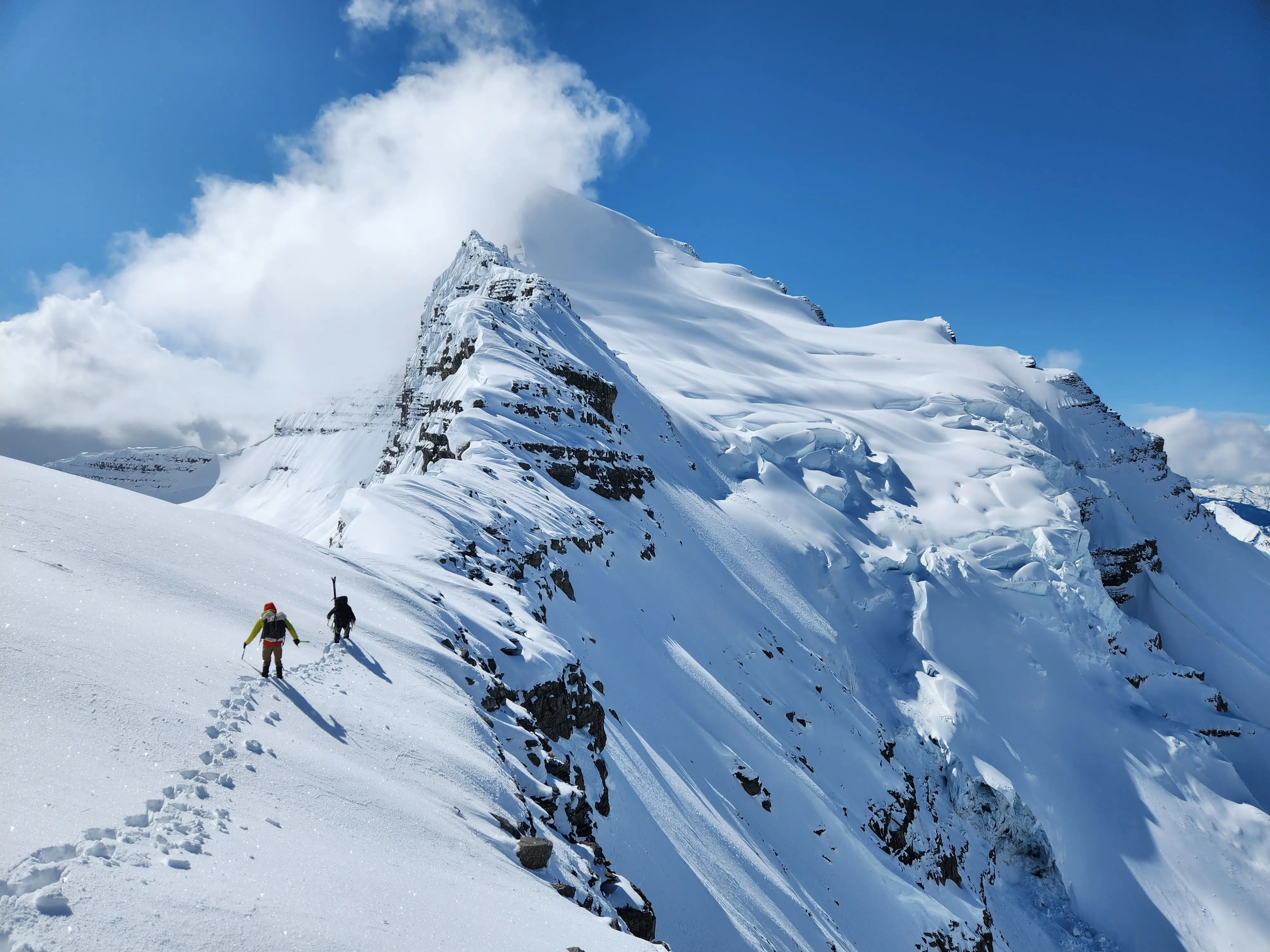 Climbers ascending the heavily crevassed north ridge of Tsar Mountain with its heavily crevassed glacier visible at right and it's snowcapped and clouded over summit above.