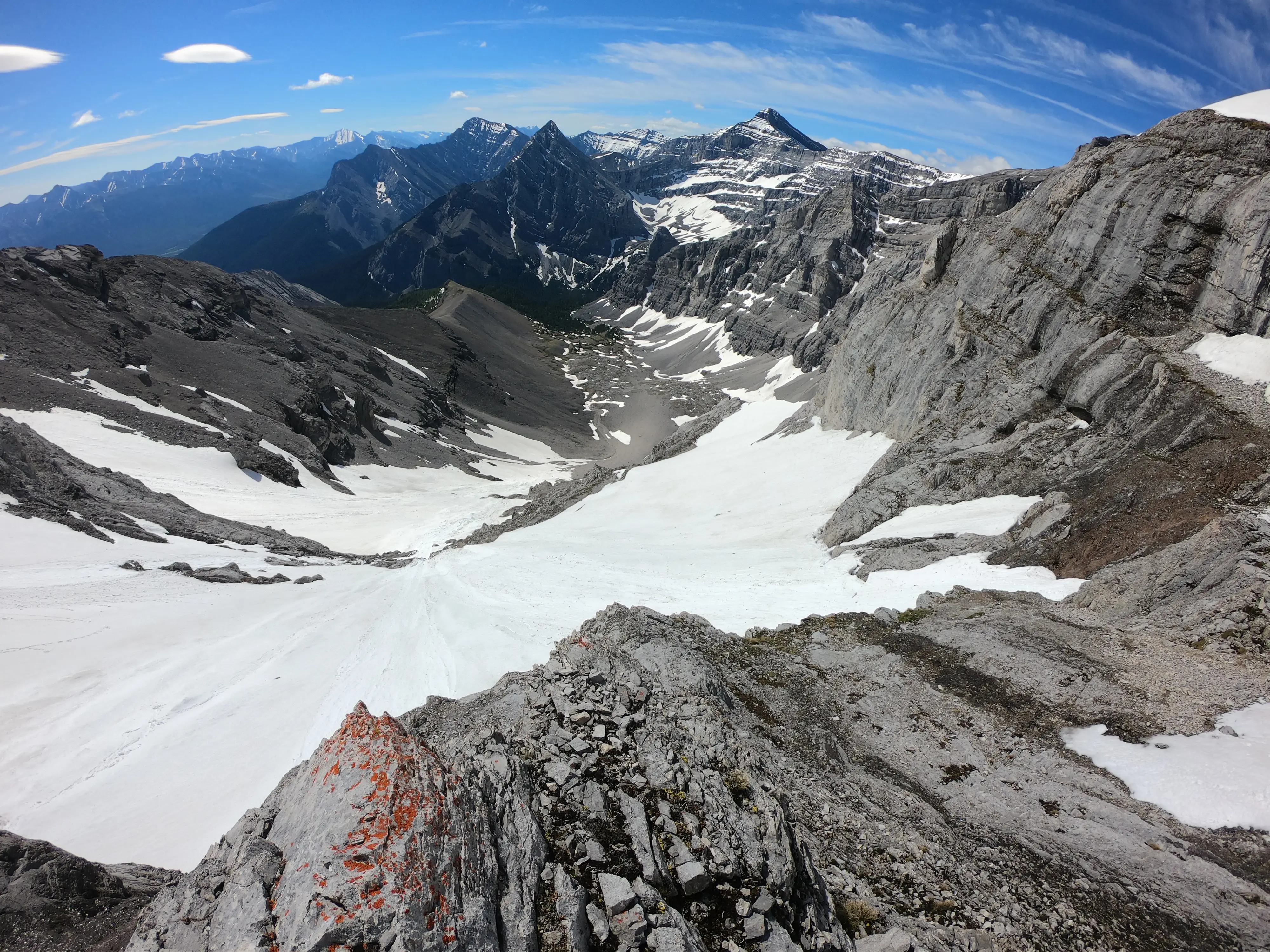 Looking down the steep snow covered terrain on Wind Mountain during the ascent, with rugged limestone walls and dramatic alpine terrain stretching toward distant peaks.